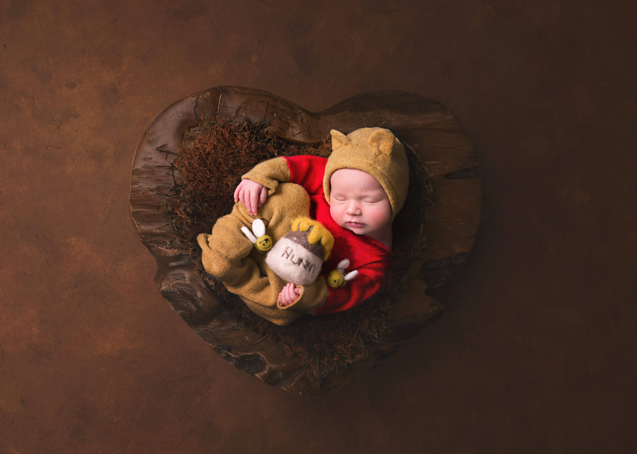 Adorable little newborn baby dressed in a bear outfit holding a honey pot in a wooden bowl at her Newborn Photoshoot in Birmingham,Newborn Photographer Birmingham